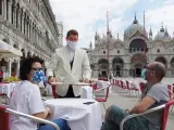 Un camarero sirve a dos turistas en la plaza de San Marcos en Venecia (Italia).