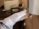 Un trabajador protegido con mascarilla coloca gel desinfectante en un dispensador para clientes