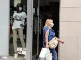 Una mujer camina con mascarilla y bolsas de la compra, delante de un escaparate donde el maniquí también lleva, en Mollerussa (Lleida).