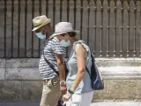 Dos personas pasean con mascarilla y sombrero en Sevilla.