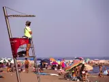 Un socorrista con mascarilla observa atentamente a los ba&ntilde;istas en la playa de la Malagueta de M&aacute;laga.