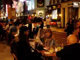 Una camarera con mascarilla por el coronavirus atiende una mesa en una terraza de un restaurante en Londres, Reino Unido.
