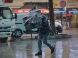 Una persona camina bajo la lluvia en un día con rachas de viento en Madrid.