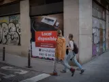 Dos personas caminan por una calle del Barrio Gótico ante un local cerrado en Barcelona.