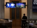 Una persona camina bajo los televisores indicativos con los valores del Ibex en el Palacio de la Bolsa de Madrid.