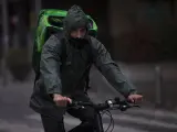 Un rider (repartidor) trabaja bajo la lluvia protegido con un impermeable
