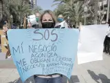 Una mujer perteneciente al sector hostelero de Alicante sostiene una pancarta en una manifestación.