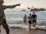 Varios menores migrantes salen del agua ante las indicaciones de un militar español.