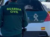 Un agente de la Guardia Civil de espaldas y junto a un vehículo oficial del cuerpo.