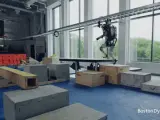 El robot Atlas apoya una mano en una viga de madera para saltarla elevando las piernas.