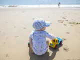 Baby boy playing on the sand while his sister run beside beach shore. El Rompido, Cartaya, Huelva, Spain
