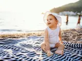Baby girl sitting on towel at the beach in summer