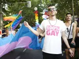 Un joven viste una camiseta en la que se lee "100% Gay" mientras sostiene una bandera trans en el Orgullo LGTBIQ+ de Madrid.