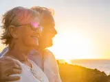 couple of two cute seniors together enjoying summer and having fun at the beach looking at the sea or ocean with sunset - mature people having a good lifestyle