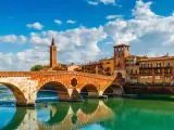 Bridge Ponte Pietra in Verona on Adige river, Veneto region, Italy. Sunny summer day panorama and blue sky with clouds. Ancient european terracotta color houses.