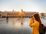 Young female tourist with camera and backpack photographing Cloth Hall in the old city center of Krakow