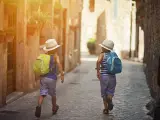 Three kids running and having fun in the beautiful mediterranean town. Little boys are wearing backpacks and hats. Kids are either tourists or are late for school.