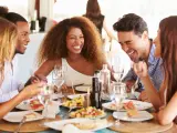 Grupo de j&oacute;venes amigas disfrutando de comida en el restaurante al aire libre riendo