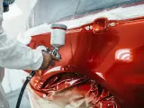 Hombre con ropa de protección y mascarilla pintando un coche con un compresor de pulverización.