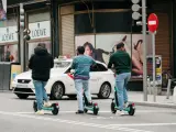 Tres personas pilotando un patinete eléctrico por una calle de Madrid.