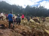 Varias personas cruzan la zona del deslizamiento de tierra para llegar al otro lado en la aldea de Yambali, en Papúa Nueva Guinea.