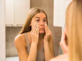 Una mujer observa sus ojeras en el espejo.