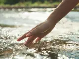 Una persona sumerge la mano en el agua de un río.