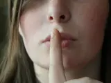 Una mujer se lleva el dedo a los labios para indicar que guarda un secreto.