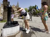 Una mujer rellena una botella en una fuente en Sevilla, en la primera ola de calor del verano de 2023