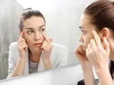 Mujer visualizando sus ojeras a trav&eacute;s del espejo.