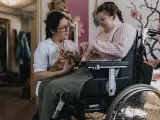 Una joven en silla de ruedas junto a su cuidadora.