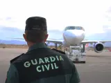 Un agente de la Guardia Civil, de espaldas, en la pista de un aeropuerto con un avión al fondo.