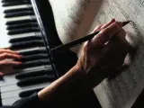 Una mujer toca el piano y escribe apuntes en una partitura.