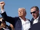 Donald Trump alza el puño con un gesto de rabia mientras es desalojado del escenario.