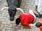 Un mozo cae junto a uno de los toros en el último encierro de los Sanfermines 2024.