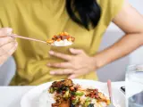 Una mujer se toca el estómago con una mano mientras come con la otra.
