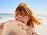 Mujer al sol en la playa sosteniendo un sombrero.