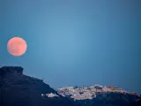 The moon rises from behind the village of Fira on the Greek island of Santorini, on July 20, 2024. (Photo by Aris Oikonomou / AFP)